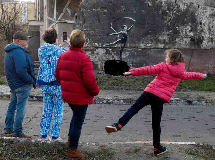 Una famiglia osserva un murale che ricorda le opere di Banksy, su un muro di un edificio distrutto a Borodyanka. Sarebbe diverse, in varie zone dell'Ucraina, le opere attribuite all'artista di strada britannico. Foto Ansa/Epa Sergey Dolzhenko