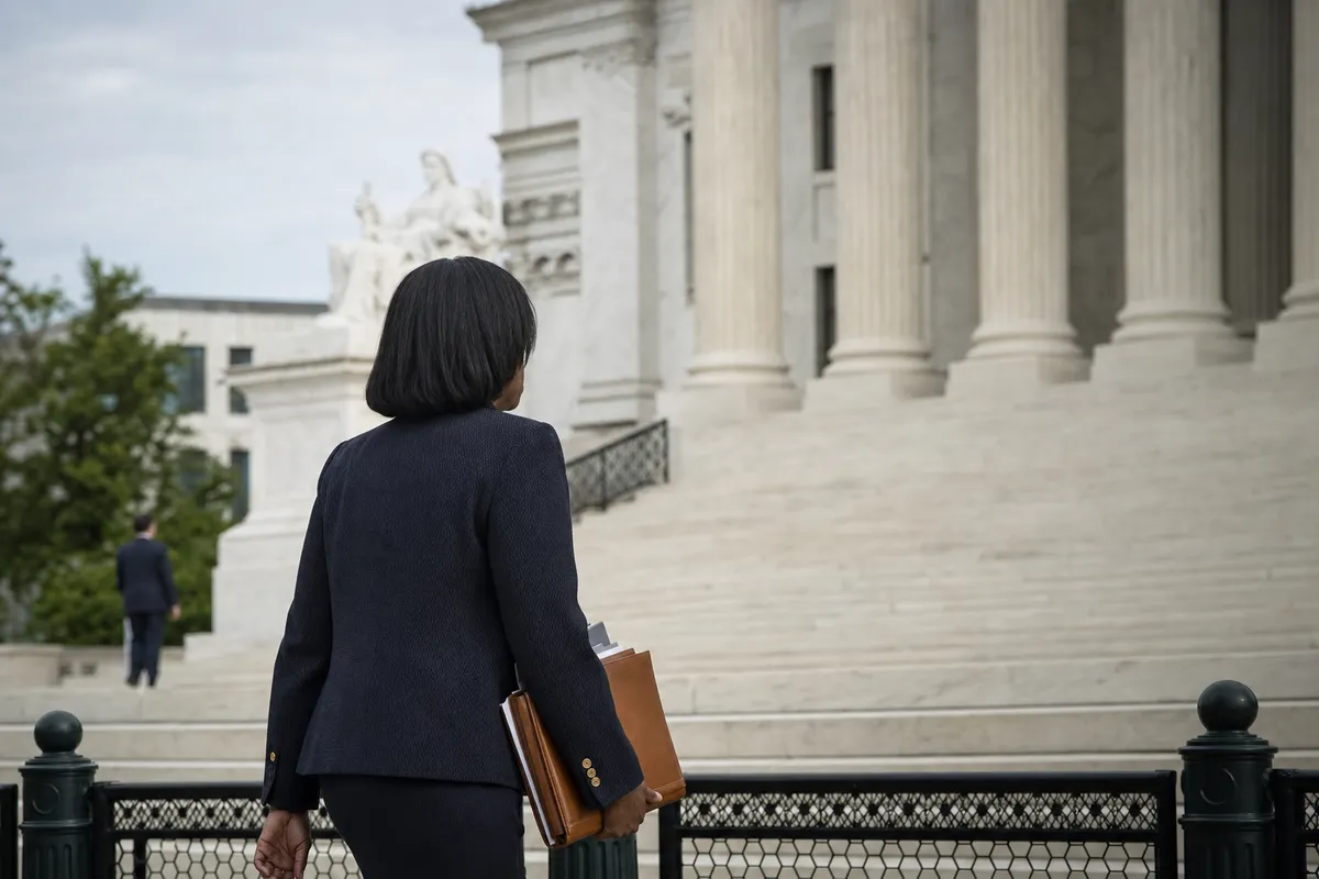 Donna in abito scuro con cartella in mano sale i gradini di un tribunale con colonne di marmo